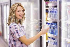 Portrait of a smiling pretty blonde woman taking a water bottle