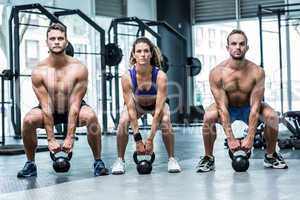 Three muscular athletes about to lift a kettle bell