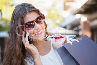 Smiling woman with sunglasses and shopping bags calling