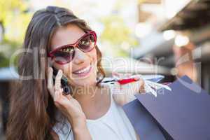 Smiling woman with sunglasses and shopping bags calling