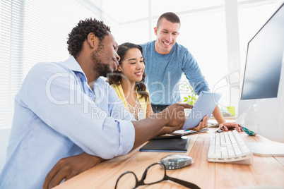 Smiling coworkers using tablet computer together and pointing th
