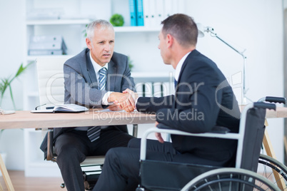 Businessman in wheelchair shaking hands with colleague