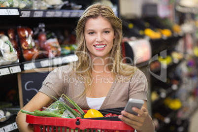 Portrait of smiling blonde woman buying vegetables and using her