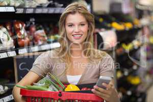 Portrait of smiling blonde woman buying vegetables and using her