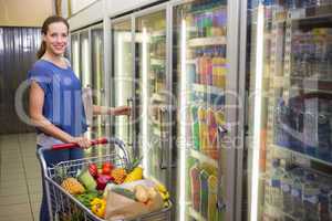 Pretty woman looking at camera and taking product on fridge