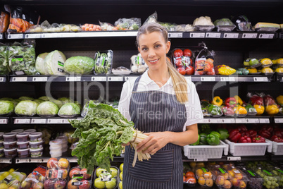 Pretty blonde woman holding vegetable and looking at camera