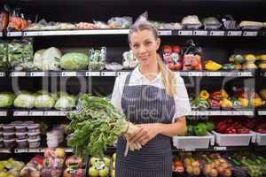 Pretty blonde woman holding vegetable and looking at camera