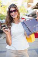 Portrait of smiling woman with sunglasses and shopping bags usin