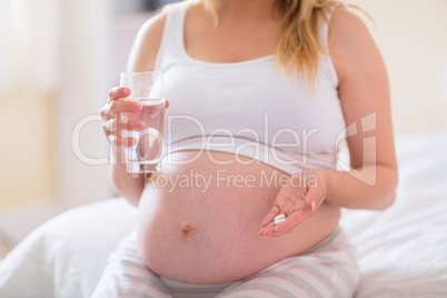 Pregnant woman sitting on bed  and holding glass of water