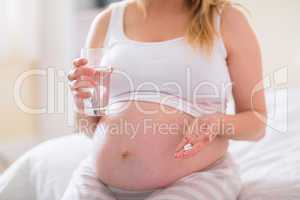 Pregnant woman sitting on bed  and holding glass of water