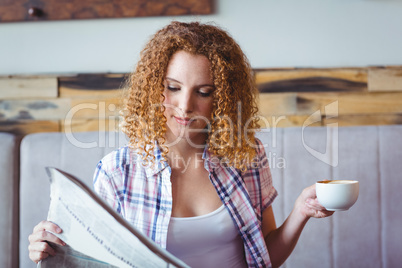 Pretty curly hair girl having cup of coffee and reading newspape