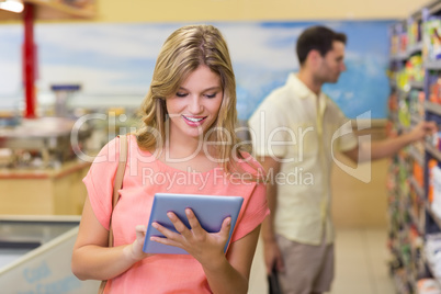 Smiling pretty blonde woman using digital tablet and buying prod