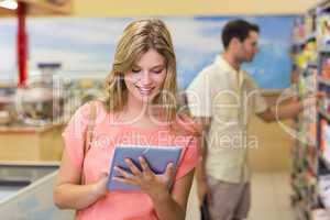 Smiling pretty blonde woman using digital tablet and buying prod