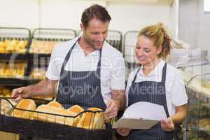 Smiling bakers looking at notepad and holding a basket with brea