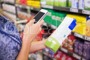 Woman comparing the price of a carton of milk with her phone