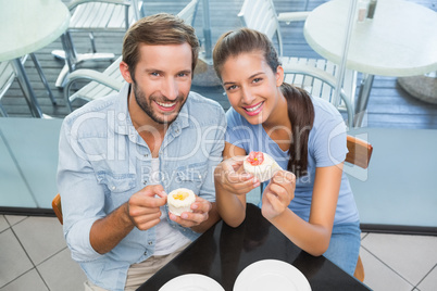 Young happy smiling couple eating cake while looking at the came