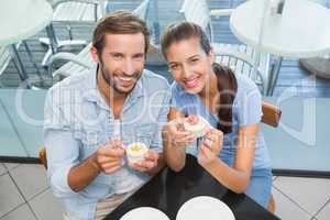 Young happy smiling couple eating cake while looking at the came