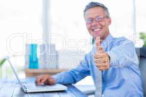 Happy businessman using laptop computer and looking at camera wi