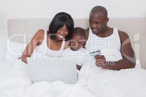 Pretty couple using laptop with his son in bed together