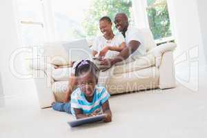 Pretty couple using laptop on couch and their daughter using tab