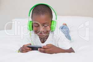 Pretty little boy using smartphone and listening music in bed