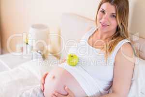 Pregnant woman lying on bed with apple in belly