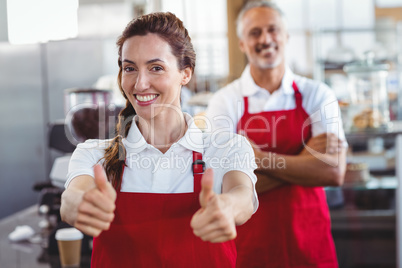 Smiling barista gesturing thumbs up with colleague behind