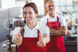 Smiling barista gesturing thumbs up with colleague behind