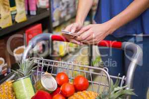 Pretty woman pushing trolley in aisle and texting