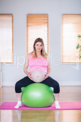 Pregnant woman touching her belly on exercise ball