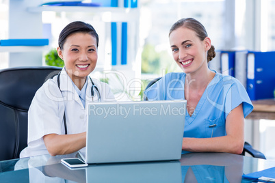 Doctor and nurse looking at laptop and smiling at camera