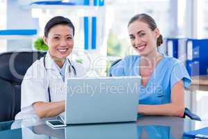 Doctor and nurse looking at laptop and smiling at camera