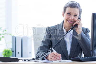 Smiling portrait of a businesswoman phoning and writing