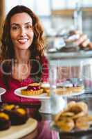 Pretty brunette smiling at camera behind plates of pastries