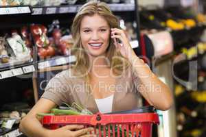 Portrait of smiling blonde woman buying vegetables and phoning