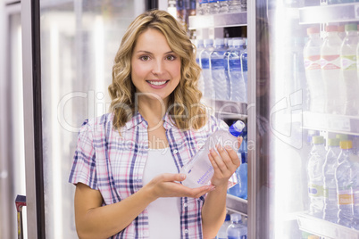 Portrait of a smiling pretty blonde woman taking a water bottle