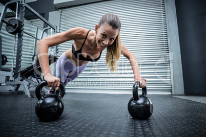 Muscular woman doing pushups with kettlebells