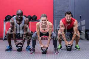 Three muscular athletes about to lift a kettle bell