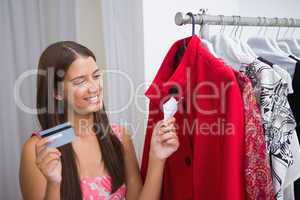 Smiling woman looking at red coat and holding credit card