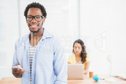 Smiling man posing in front of his colleague with smartphone