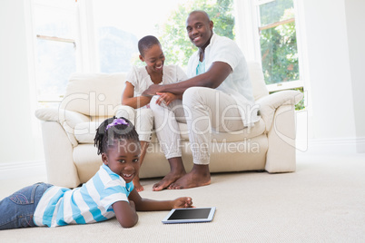 Pretty couple sitting on couch and their daughter using digital