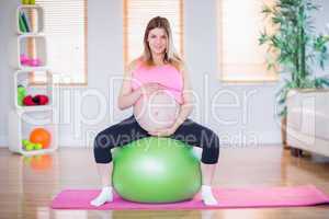 Pregnant woman touching her belly on exercise ball