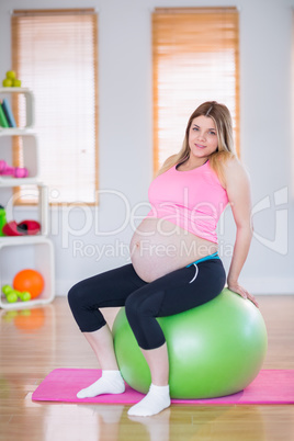 Pregnant woman looking at camera sitting on exercise ball