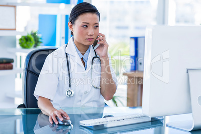 Concentrated doctor having phone call and using her computer