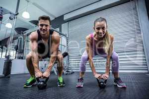 A muscular couple lifting kettlebells