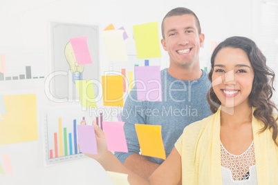 Portrait of smiling coworkers pointing sticky notes and looking