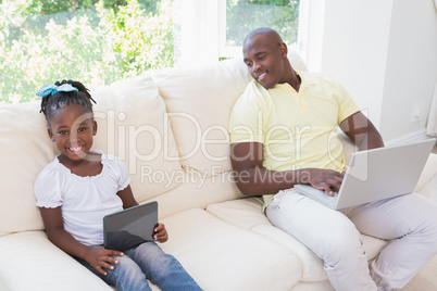 Happy smiling father using laptop and her daughter using tablet