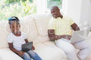 Happy smiling father using laptop and her daughter using tablet