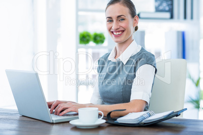 Happy businesswoman working on laptop computer and looking at ca