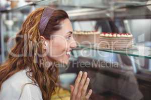 Pretty brunette looking at cakes through the glass